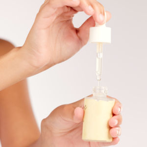 Hand die een exfoliant met pipet uit een glazen flesje haalt.