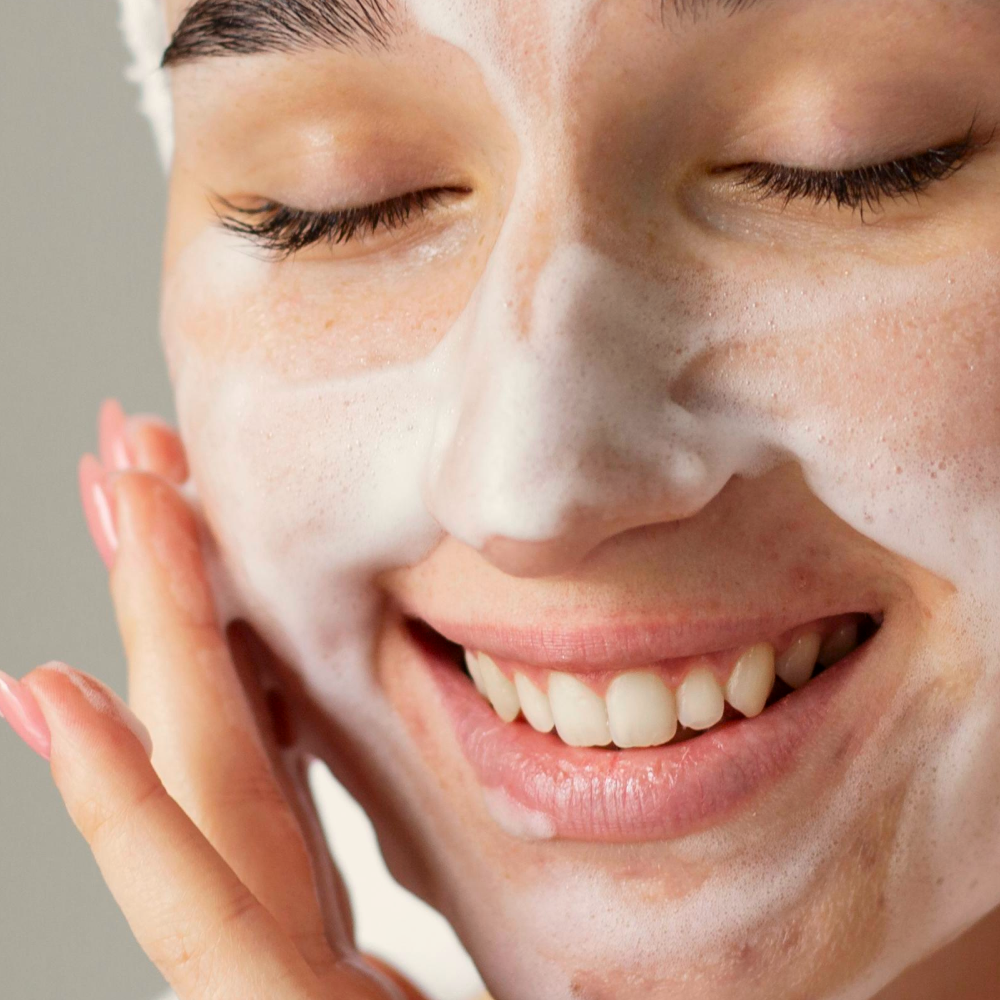 Vrouw met gesloten ogen reinigt haar gezicht met schuimende gezichtsreiniger.